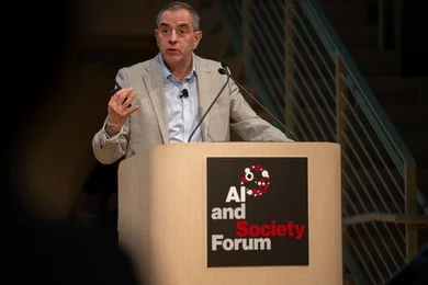 David Autor speaks from a lectern that has a sign reading "AI and Society Forum."