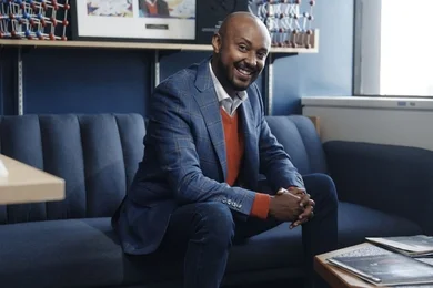 Iwnetim Abate poses seated on a blue couch in a small office