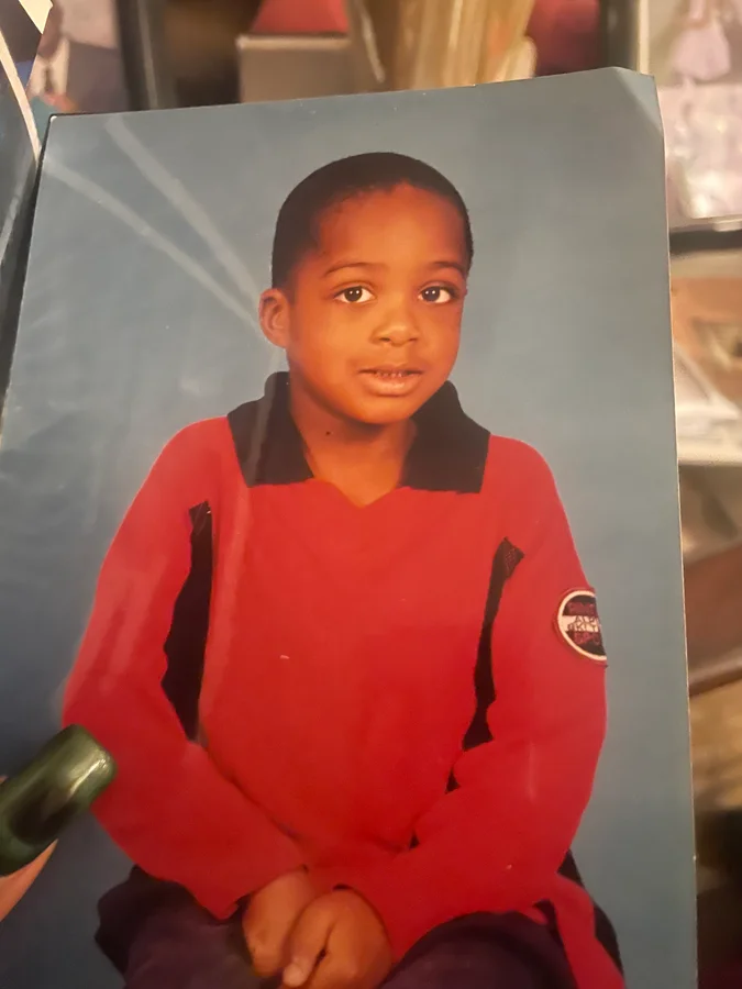 A photograph of a printed studio portrait shows a young child wearing a red shirt with a black collar, seated against a blue background.