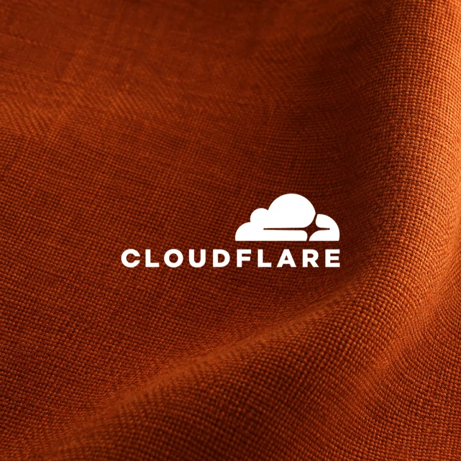 White Cloudflare cloud symbol and wordmark over folded burnt-orange woven fabric.